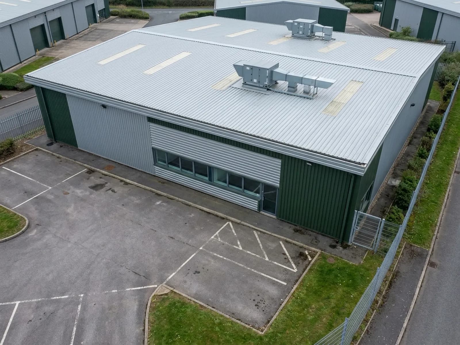 A modern light industrial unit on a Devon business park photographed from the air, showing the metal roof and rooftop plant, the profiled cladding on the elevation and the box gutter and service yard below